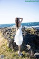 A woman in a white dress standing on a rocky beach.