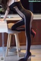 A woman in a black bodysuit sitting on a stool.