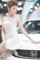 A woman in a white dress leaning on a white car.