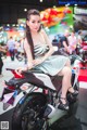 A woman sitting on a motorcycle at a motorcycle show.