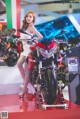 A woman in a white dress standing next to a red motorcycle.