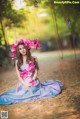 A woman in a blue dress sitting on a swing with flowers in her hair.