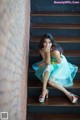 A woman in a blue dress sitting on a set of stairs.