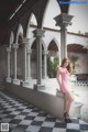 A woman in a pink dress leaning against a wall.