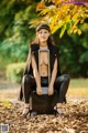 A woman sitting on top of a suitcase in a park.