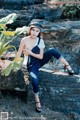 A woman sitting on top of a rock next to a plant.