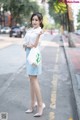 A woman in a white shirt and blue skirt is standing on the street.