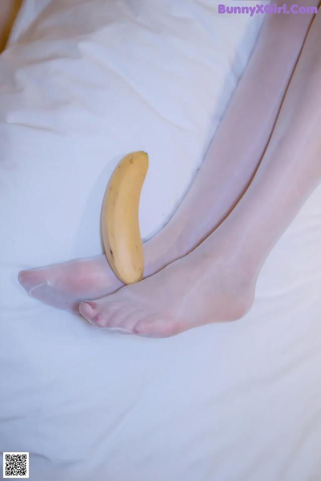 A banana sitting on top of a bed next to a woman's feet.