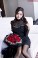 A woman sitting on a bed holding a bouquet of red roses.