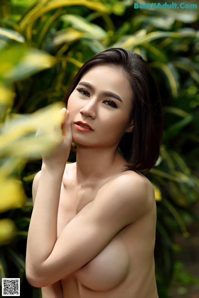 A naked asian woman posing in front of a bush.