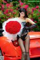 A woman holding a bouquet of red roses next to a red car.