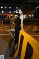 A woman in a black dress leaning on a yellow barrier.