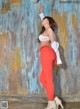 A woman in a white top and red pants posing for a picture.